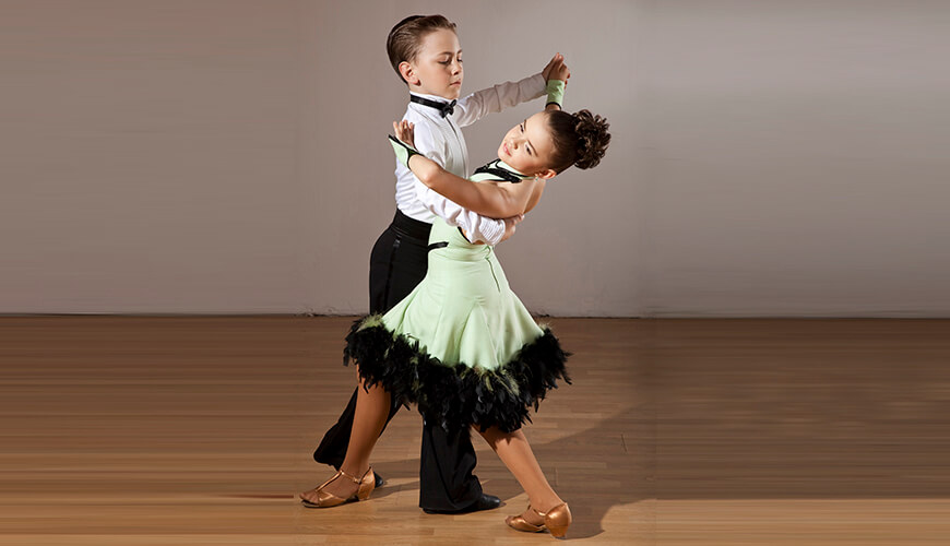 Παιδικό ζευγάρι εκτελεί χορογραφία Latin ballroom με χάρη και συγχρονισμό, αναδεικνύοντας τη συνεργασία και τον ρυθμό του χορού.